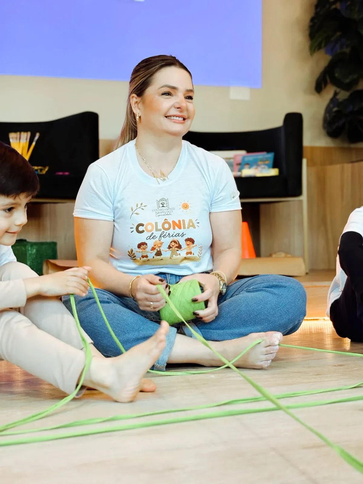 Terapeuta e crianças sentadas no chão em atividade com fio colorido no Contato Espaço Terapêutico